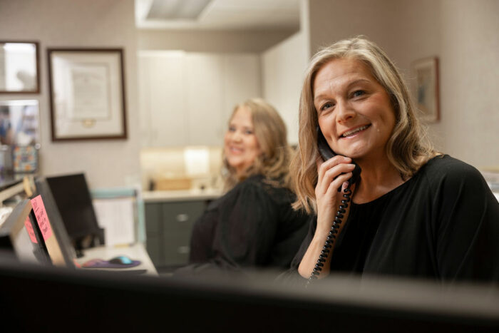 Front desk team member at Dr. Gotwalt’s Family Dentistry smiling while answering a phone call, with a colleague working in the background.